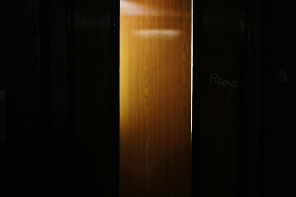 A partially open wooden door revealing light shining through a dark interior.