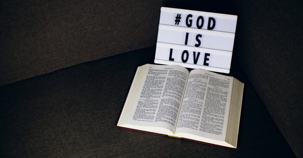 Open Bible placed beside a lightbox sign reading 'God is Love' on a dark fabric surface.